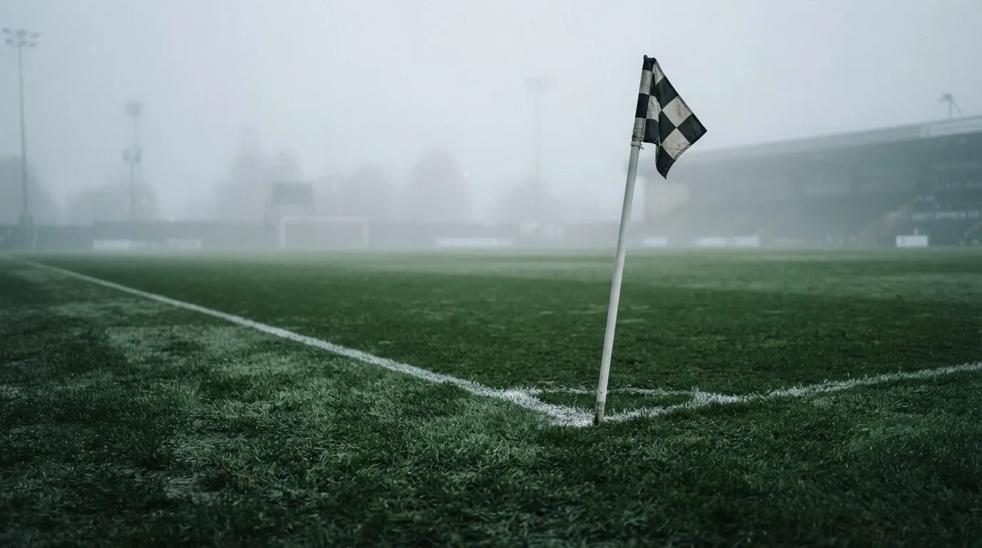 Der Rand eines Spielfelds mit weißer Linie und Eckfahne bei Nebel am frühen Morgen, ohne Menschen.