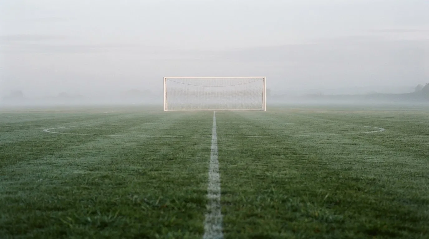 Ein Fußballtor mit Netz im Morgennebel auf einem leeren Platz, die Linien nur schwach zu erkennen.