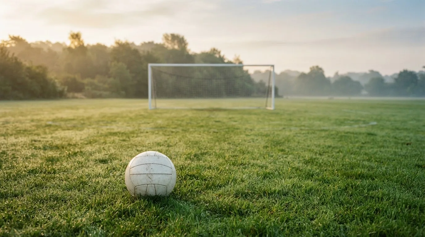 Ein Fußball auf dem Rasen vor einem leeren Tor im frühen Morgenlicht.