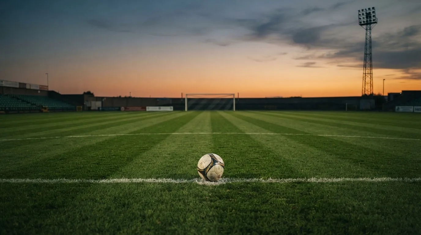 Ein Fußball liegt auf dem Elfmeterpunkt eines leeren Platzes im Abendlicht.