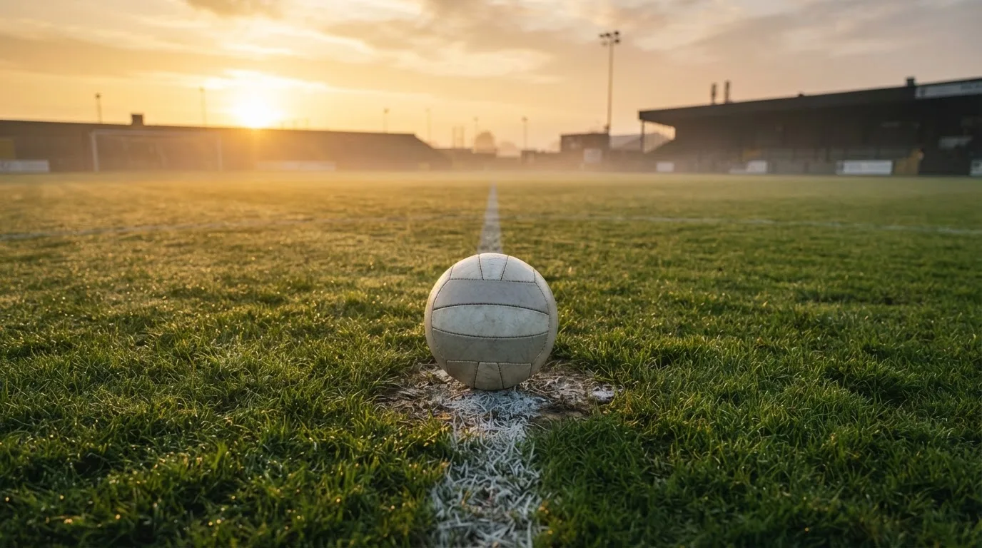 Ein Fußball auf dem Mittelkreis eines leeren Rasenplatzes im frühen Morgenlicht.