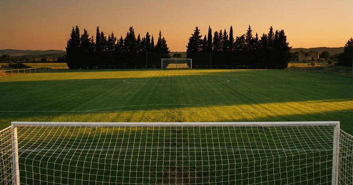 Ein Fußballtor mit Netz auf einem leeren Platz im Abendlicht, der Rasen frisch gemäht, im Hintergrund Zypressen.