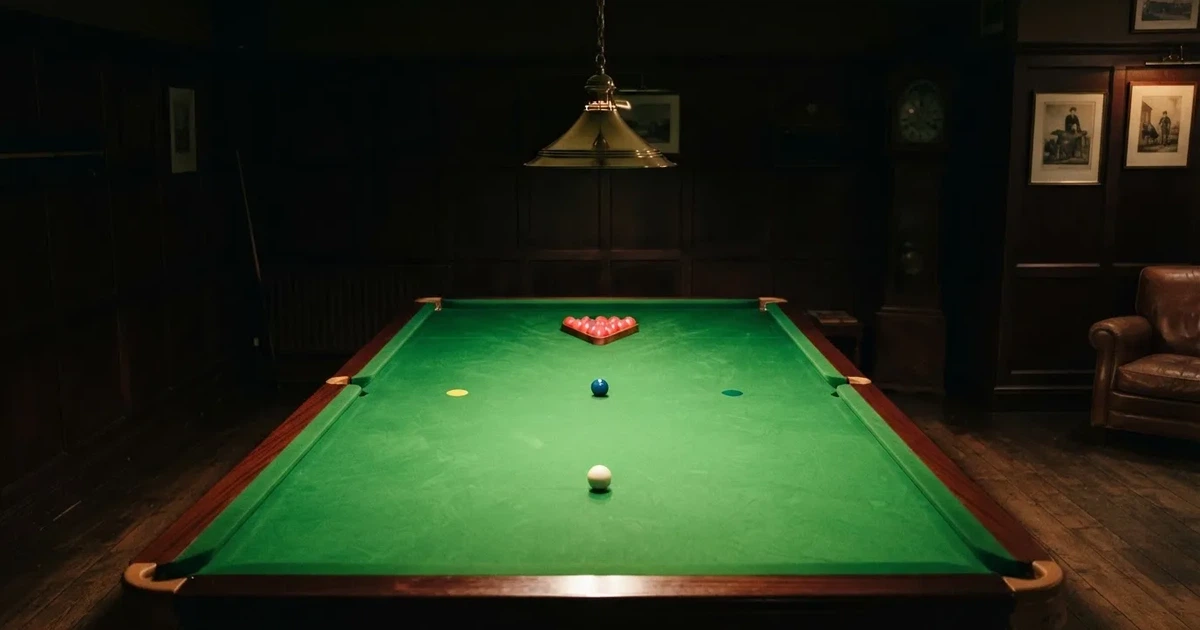 Ein Snookertisch mit grünem Tuch und aufgebauten roten Kugeln in einem abgedunkelten Raum unter einer hängenden Lampe.