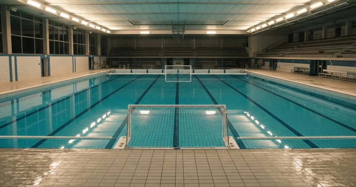 Ein Schwimmbecken mit türkisfarbenem Wasser und zwei schwimmenden Torrahmen am gegenüberliegenden Beckenrand, menschenleer unter Hallenlicht.