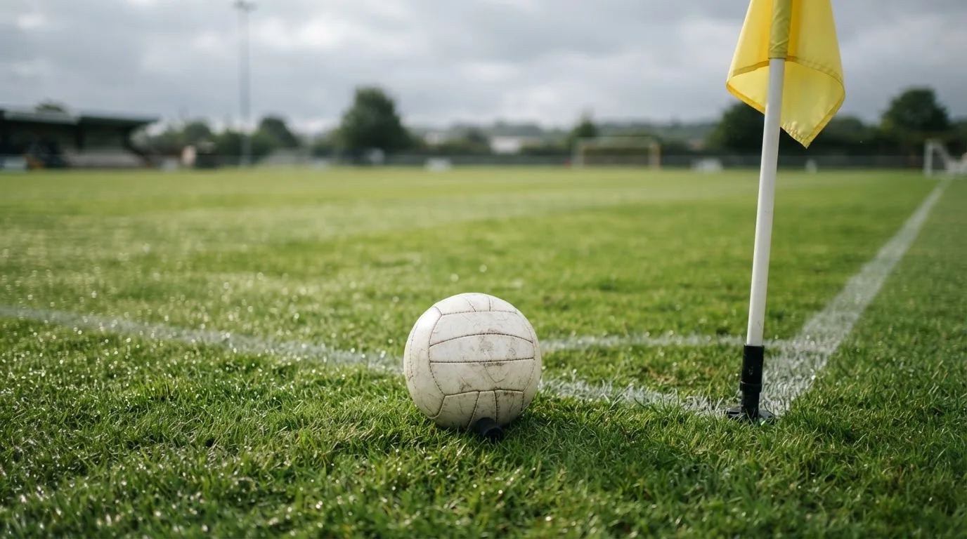 Ein Fußball liegt neben einer Eckfahne auf kurz gemähtem Rasen unter bewölktem Himmel.